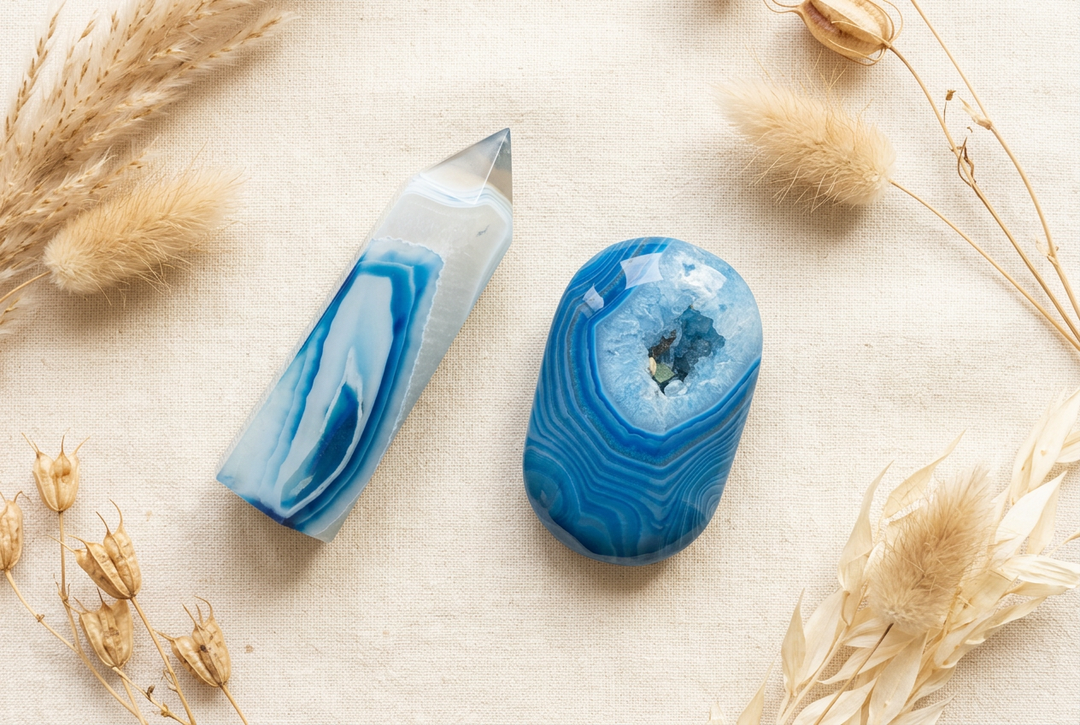 Blue banded agate pointed tower and polished palm stone with a small druzy opening on cream linen with dried botanicals.