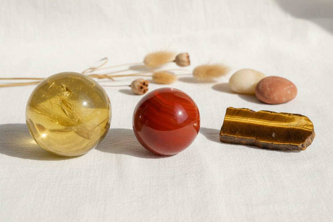 Polished citrine sphere, carnelian sphere, and tiger's eye stone with dried botanicals on white fabric.