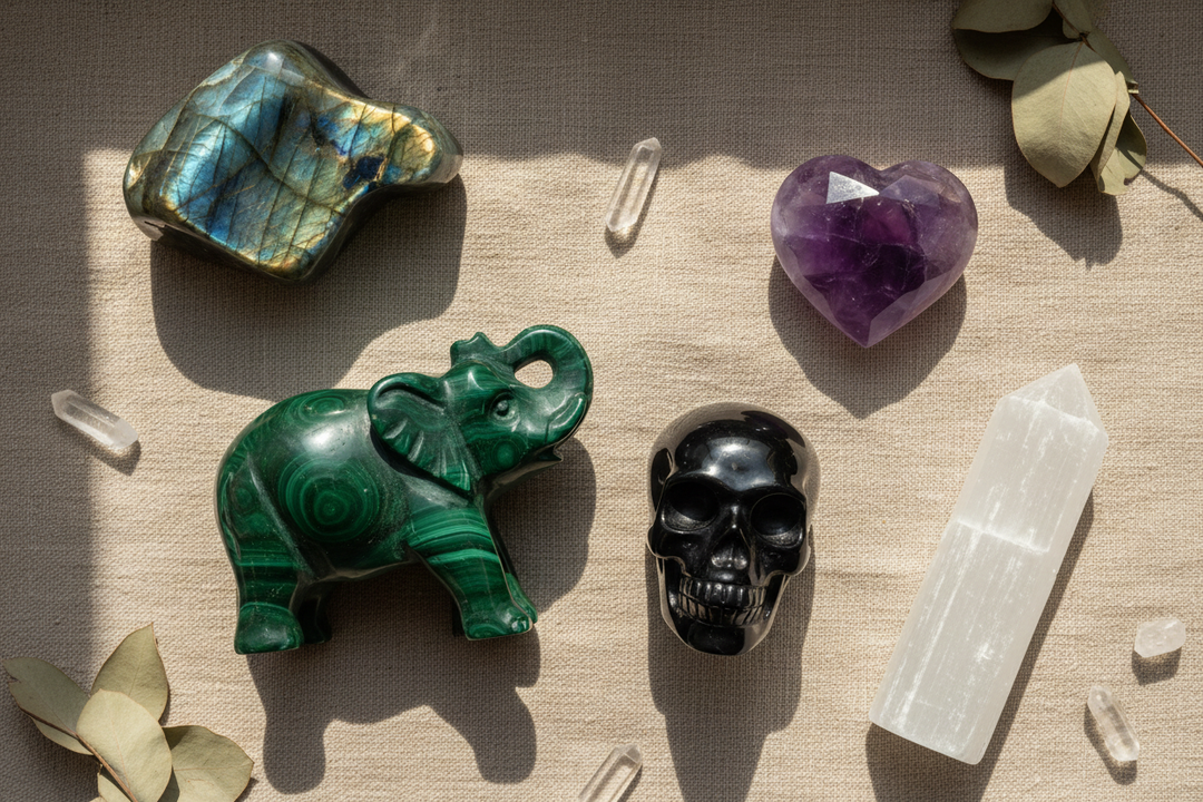 Various crystal carvings: labradorite, malachite elephant, amethyst heart, black obsidian skull, and selenite wand.