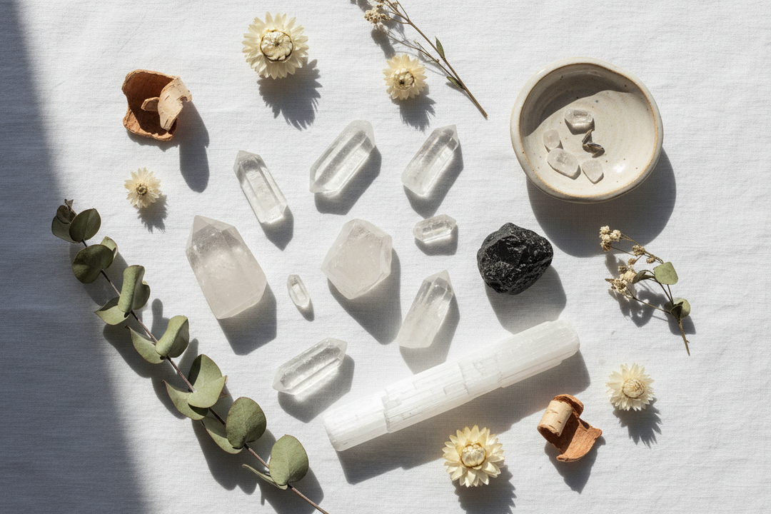 Bright lifestyle flat lay of clear quartz, selenite wand, and black tourmaline crystals on white linen with dried botanicals in natural light