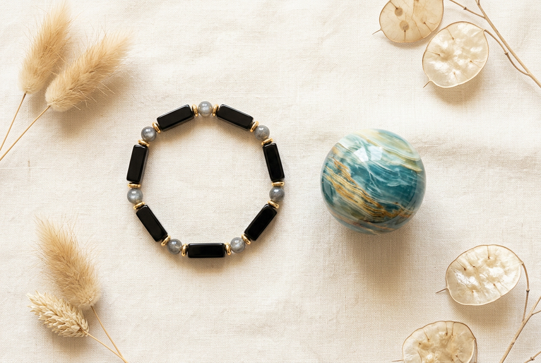 Black onyx and labradorite bead bracelet beside a polished blue onyx sphere on warm cream linen with dried botanicals.
