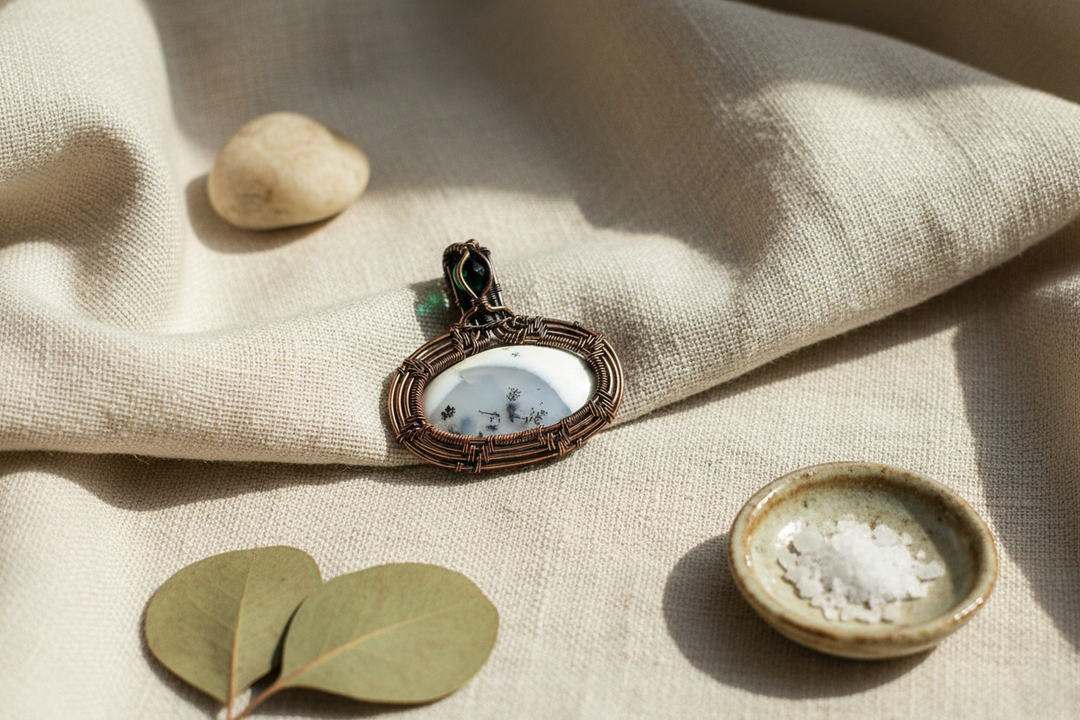Orca Agate pendant with a wire-wrapped copper setting, resting on linen with healing elements.