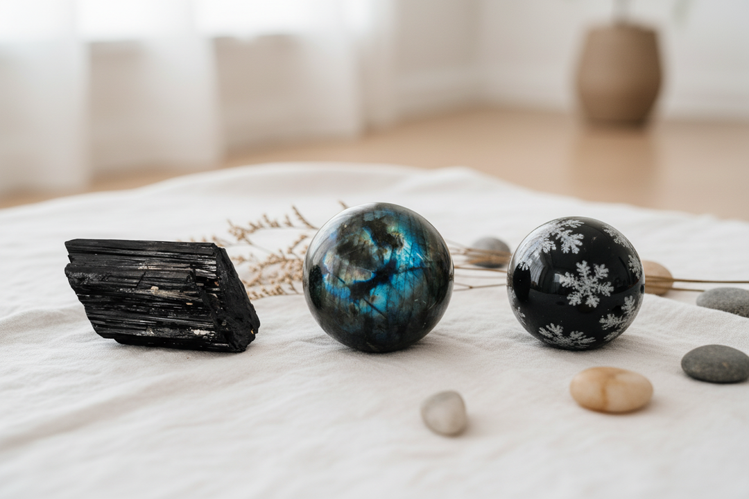 Black Tourmaline chunk, Labradorite sphere, and Obsidian sphere arranged on white linen with dried botanicals — crystals for protection and energetic shielding