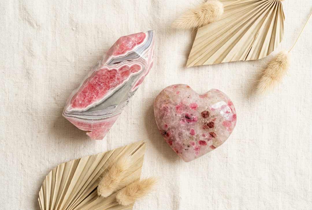 Pink banded rhodochrosite pointed tower and polished pink heart on warm cream linen with dried botanicals.
