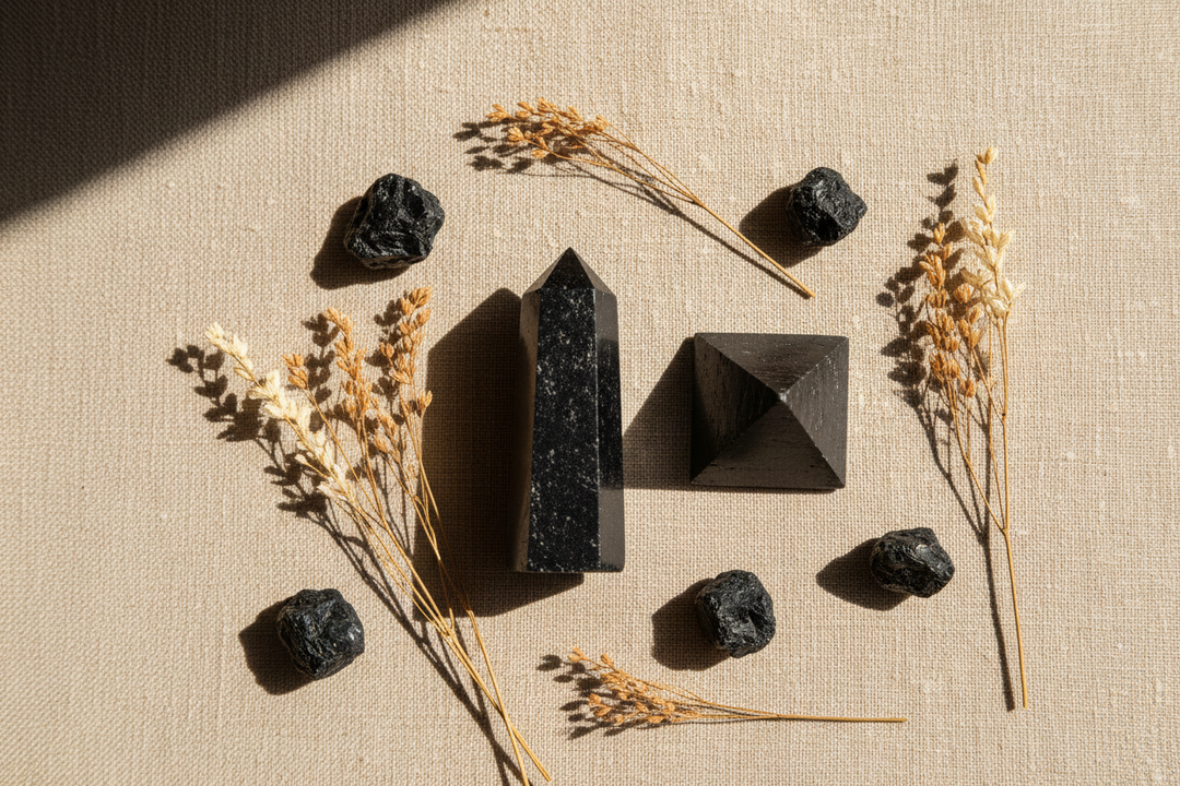 Matte black shungite tower and pyramid arranged on a warm linen surface with dried botanicals, soft natural side lighting, spa-inspired flat lay composition.