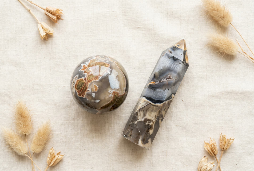 Polished volcano agate sphere and pointed tower in gray, cream and brown on warm cream linen with dried botanicals.