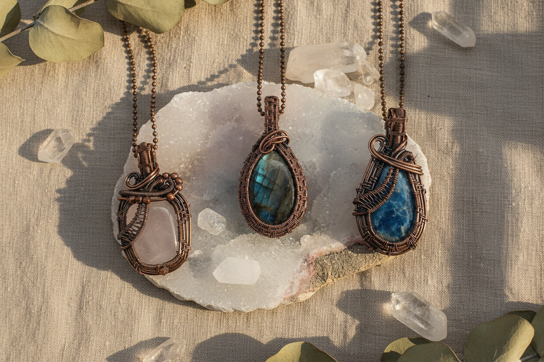 Three unique wire-wrapped crystal pendants: rose quartz, labradorite, and blue kyanite, on a quartz geode.