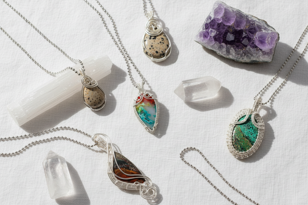 Assorted Crystal Destiny pendants and raw high vibrational crystals like amethyst and selenite on white fabric.
