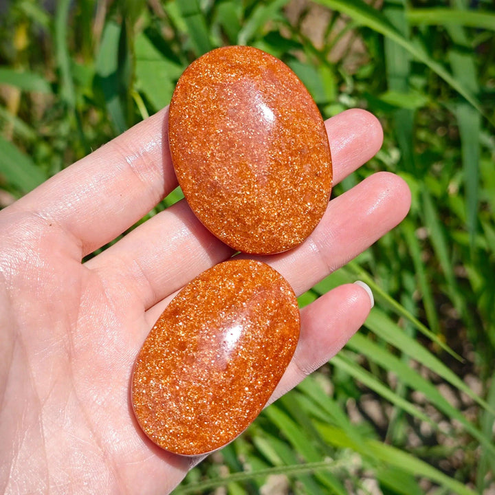 Two glittering orange Fire Sandstone palm stones held in a hand, perfect for meditation and healing.