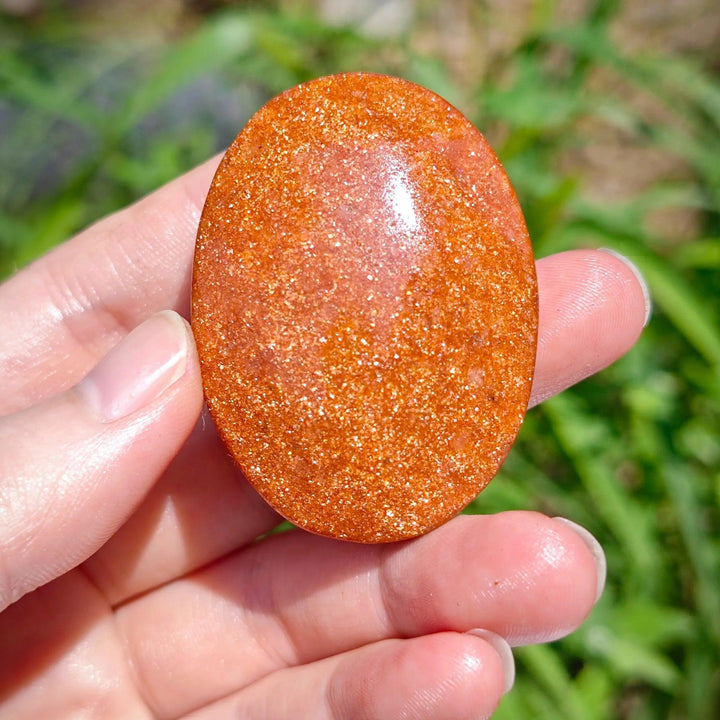 Sparkling orange Fire Sandstone Palm Stone, a polished oval crystal for meditation and healing.