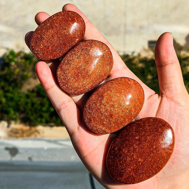 Polished orange fire sandstone palm stones with sparkling gold flecks held in a hand.