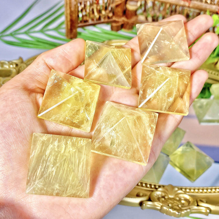 Hand holding multiple natural citrine crystal pyramids, featuring golden yellow hues and polished geometric healing energy.
