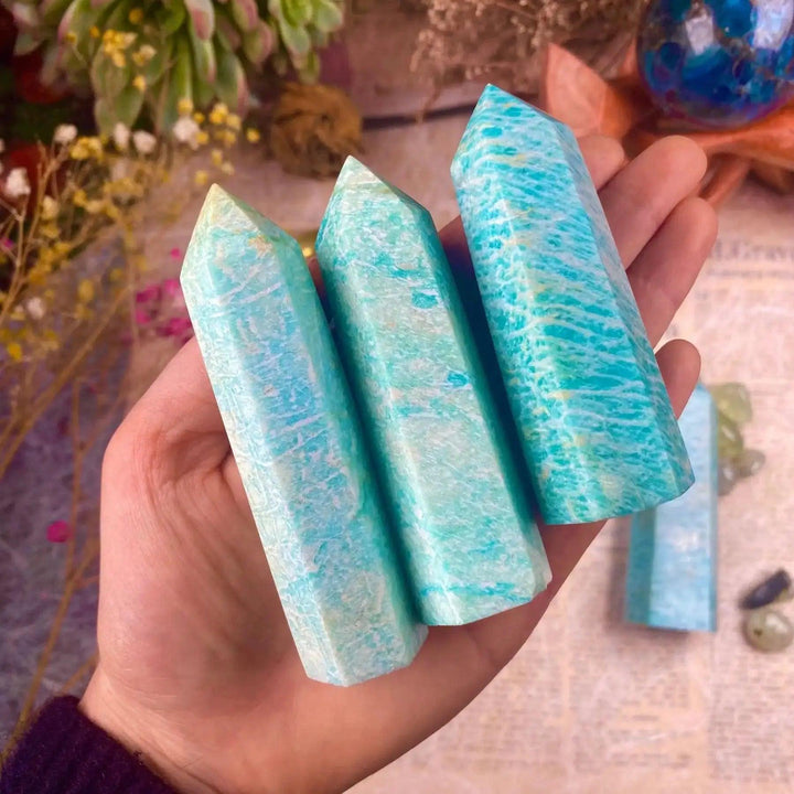 Three polished turquoise Amazonite crystal towers held in a hand, showcasing natural healing stone patterns.