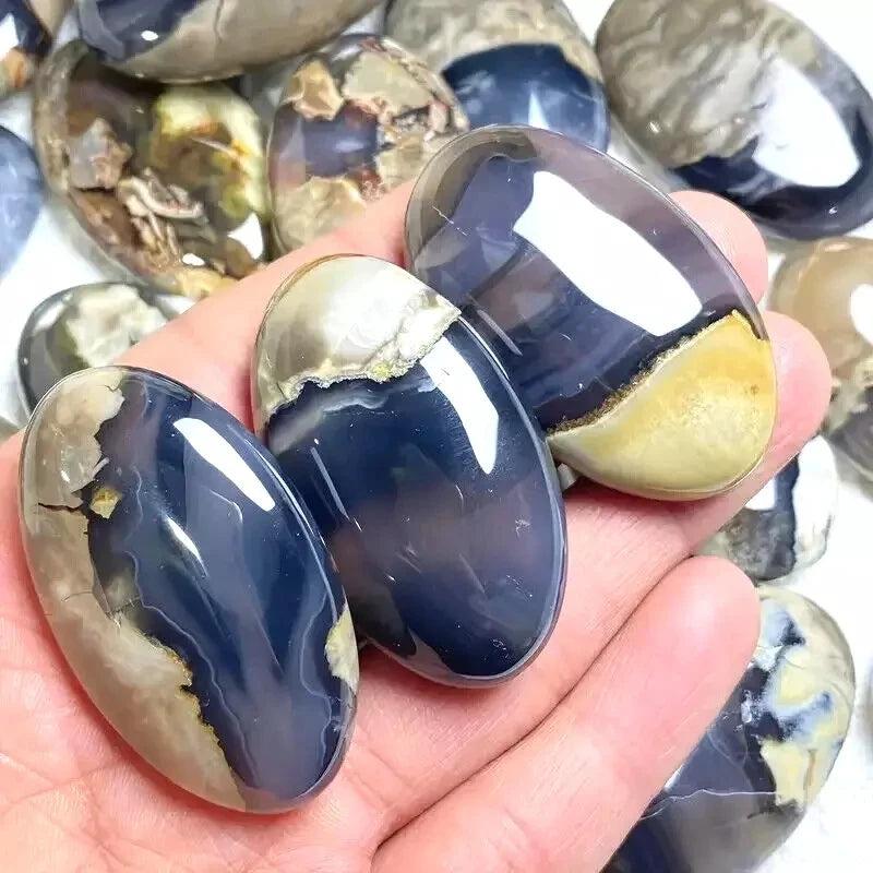 Polished natural volcanic agate palm stones in varying shades of dark blue, cream, and brown, with a smooth finish.
