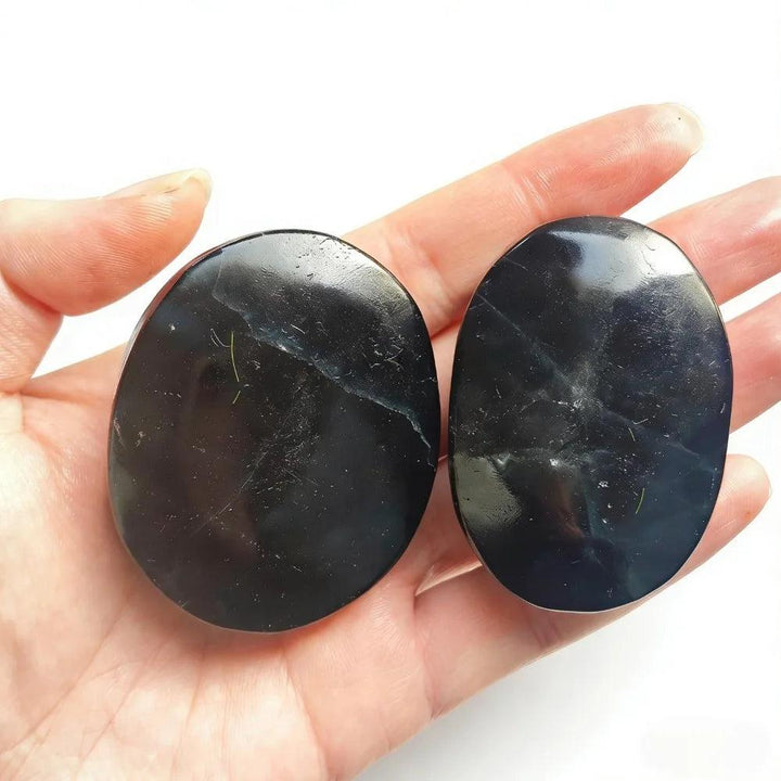 Two polished black rose fluorite crystal palm stones held in a hand, showcasing a smooth, glossy finish.