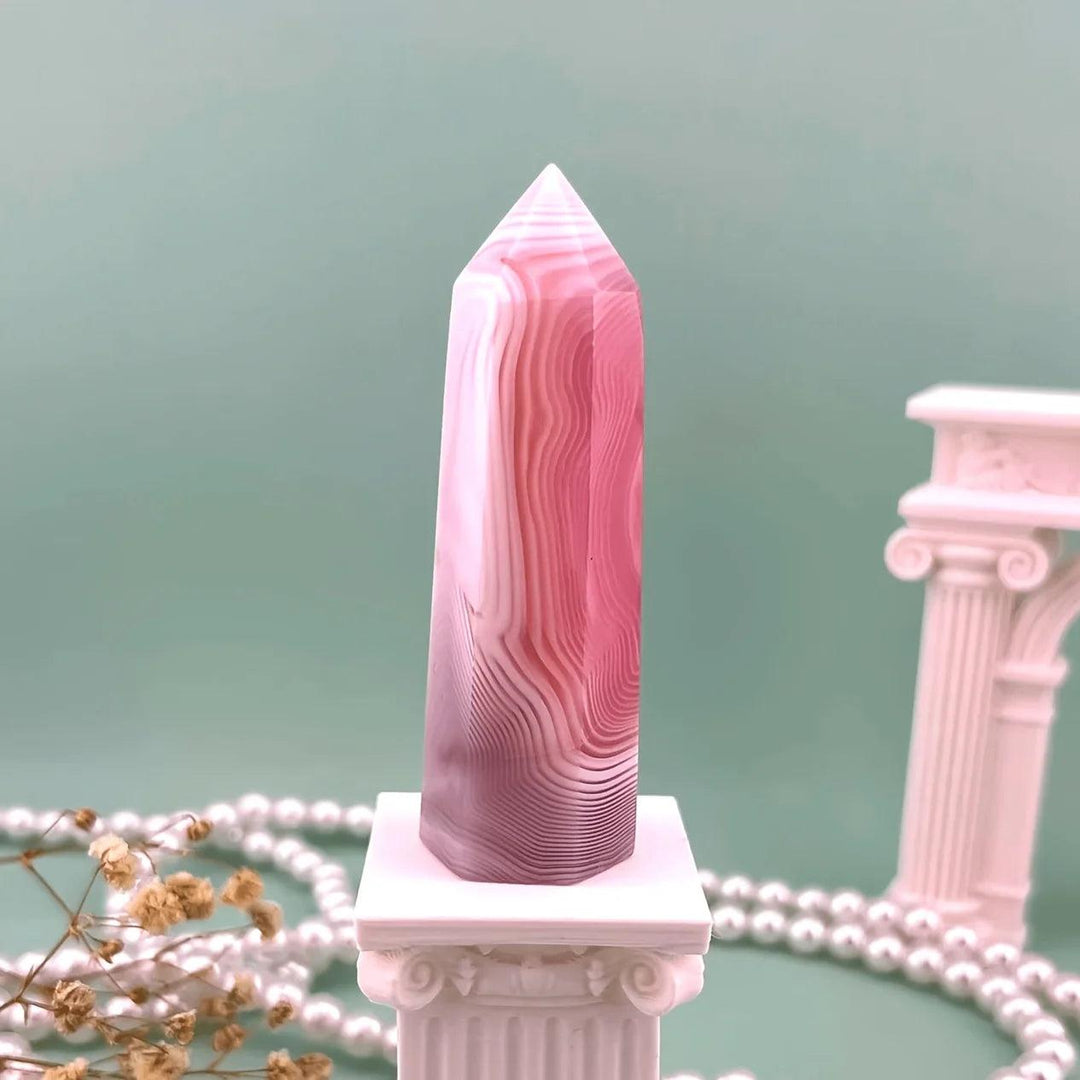 Unique pink agate pillar crystal with healing energy bands on a decorative white stand.
