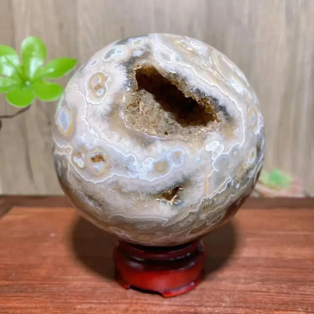 8th Vein Ocean Jasper geode sphere from Crystal Destiny, with sparkling druzy and raw texture on a red stand.