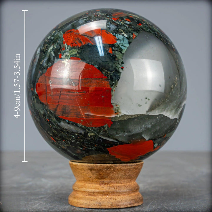 Polished African Bloodstone sphere, dark green with vivid red spots, on a wooden stand. Healing crystal.
