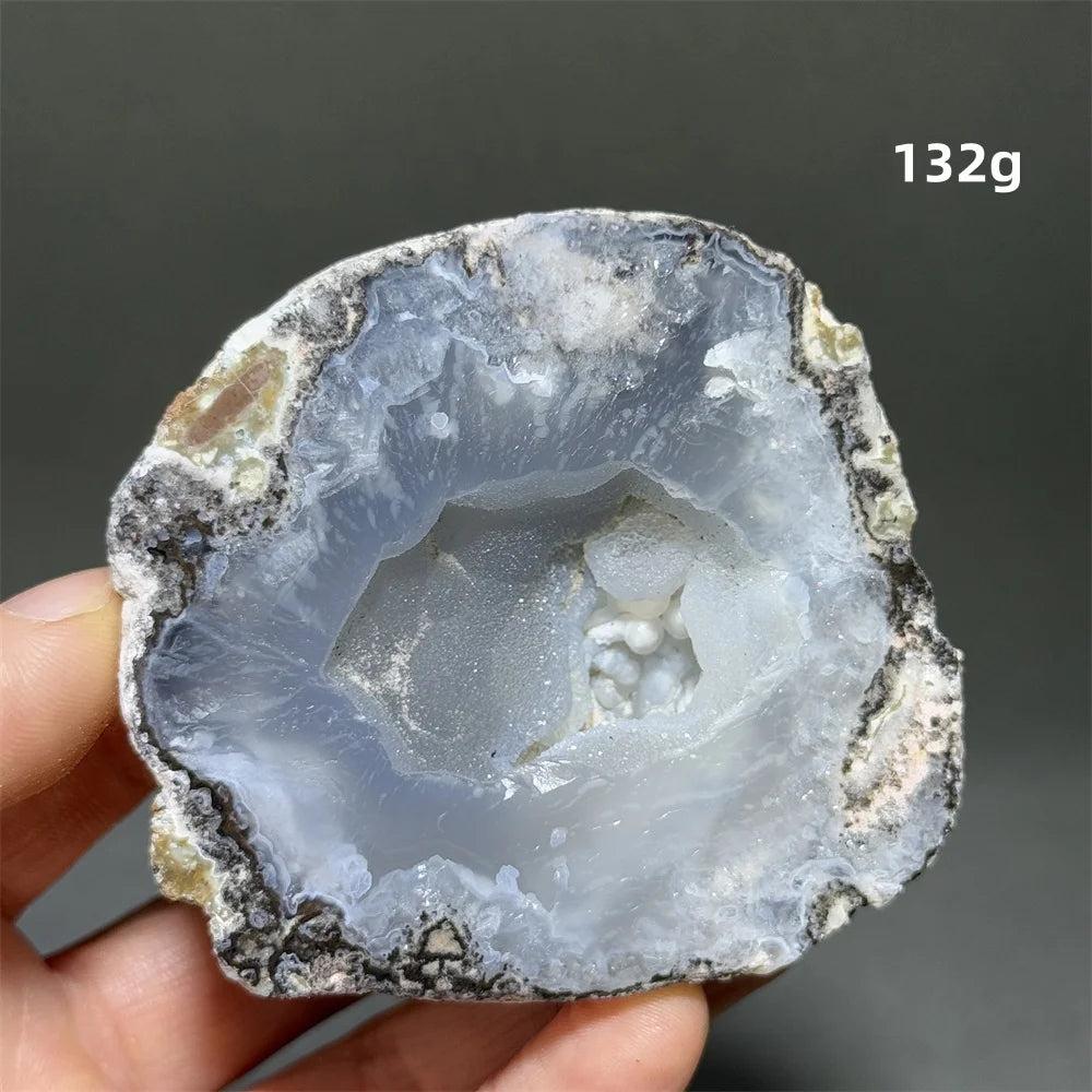 Natural Agate geode slice with a sparkling, light blue druzy crystal cave interior, held by fingers.