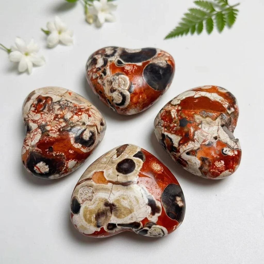 Four polished heart-shaped agate crystals with vibrant red, black, and cream patterns for grounding and healing energy.