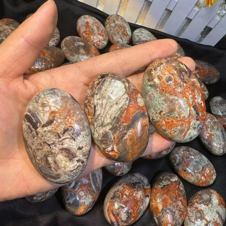 Hand holding smooth, polished agate palm stones with vibrant red, brown, and green banded patterns for grounding energy.