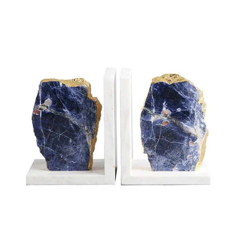 Two polished blue sodalite crystal bookends with gold edges on white marble bases.