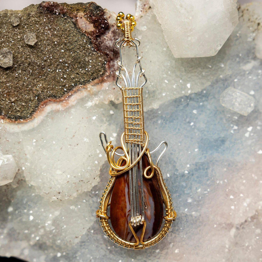 Agate Guitar Wire Wrap Pendant: Handcrafted copper guitar with a brown banded Agate crystal, symbolizing strength and harmony.