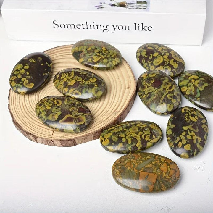 Polished Ajooba Jasper Crystal Palm Stones with grounding green and brown patterns on a wood slice.