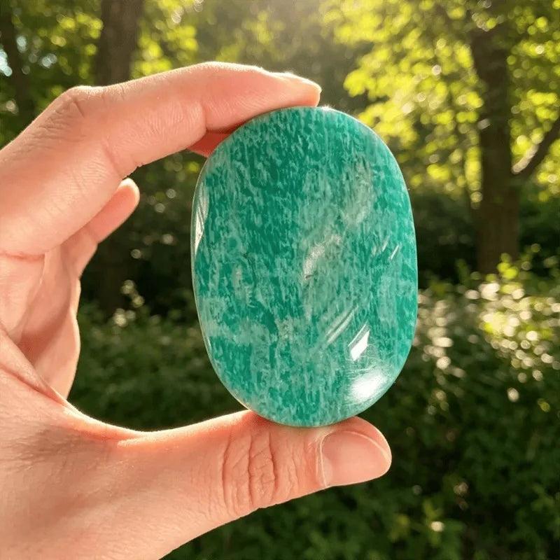 Smooth, blue-green Amazonite crystal palm stone held in hand for grounding, calming energy and heart chakra healing.
