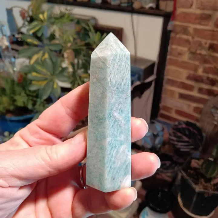 Polished light-blue Amazonite Crystal Tower held in hand, showcasing soothing natural stone patterns.