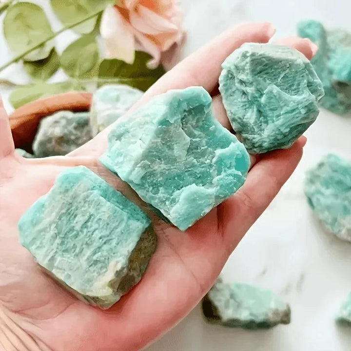 Hand holding raw Amazonite crystal chunks with natural blue-green texture for calming healing and chakra balancing.