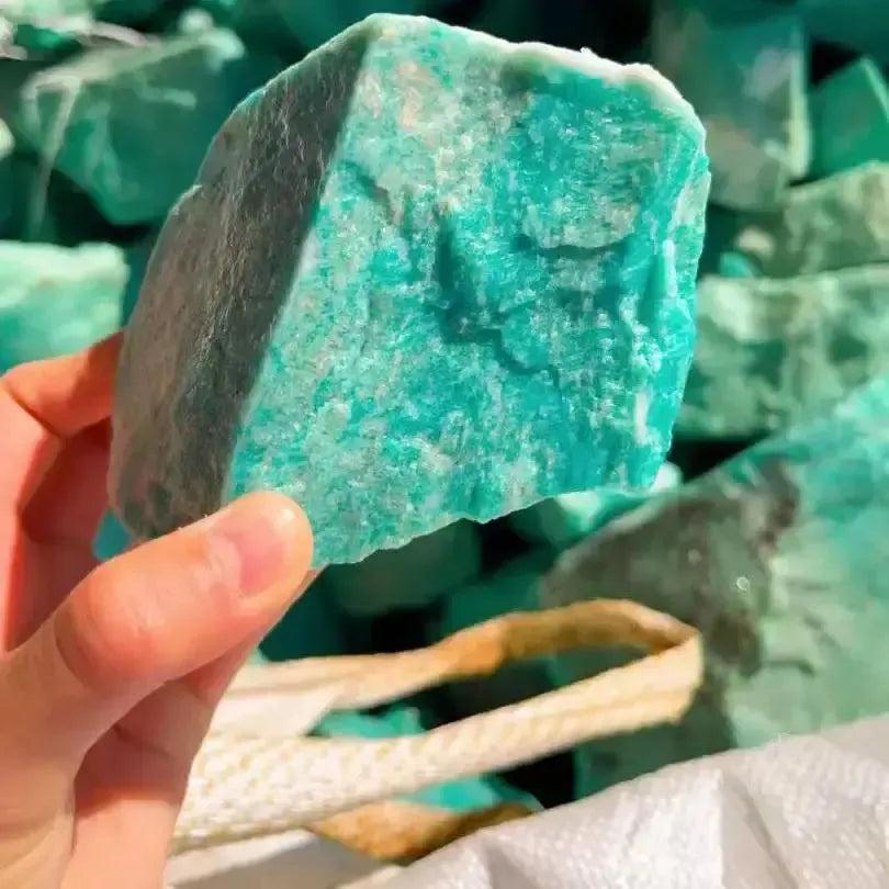 Hand holding a raw, unpolished turquoise-green Amazonite crystal from Crystal Destiny, showing its natural texture.