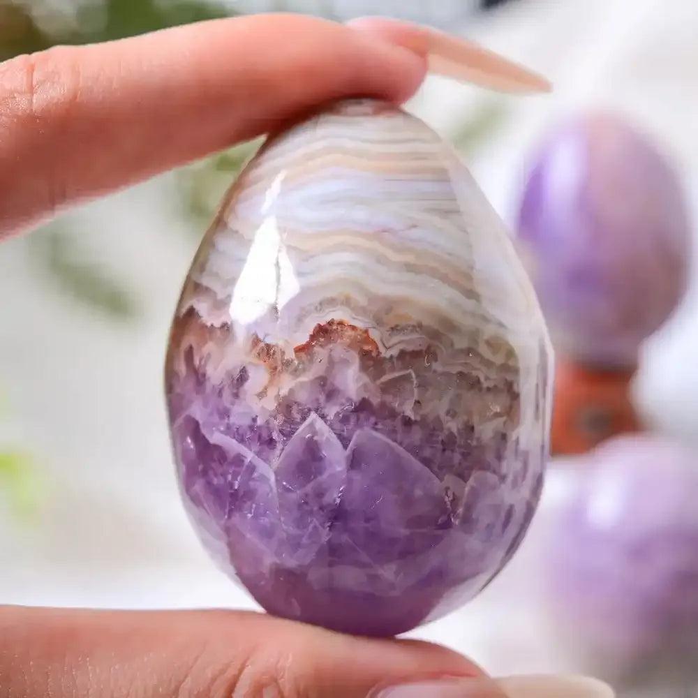 Hand-polished AAAA+ Amethyst Agate egg featuring purple crystal clusters and white, gray, and brown banded agate patterns.
