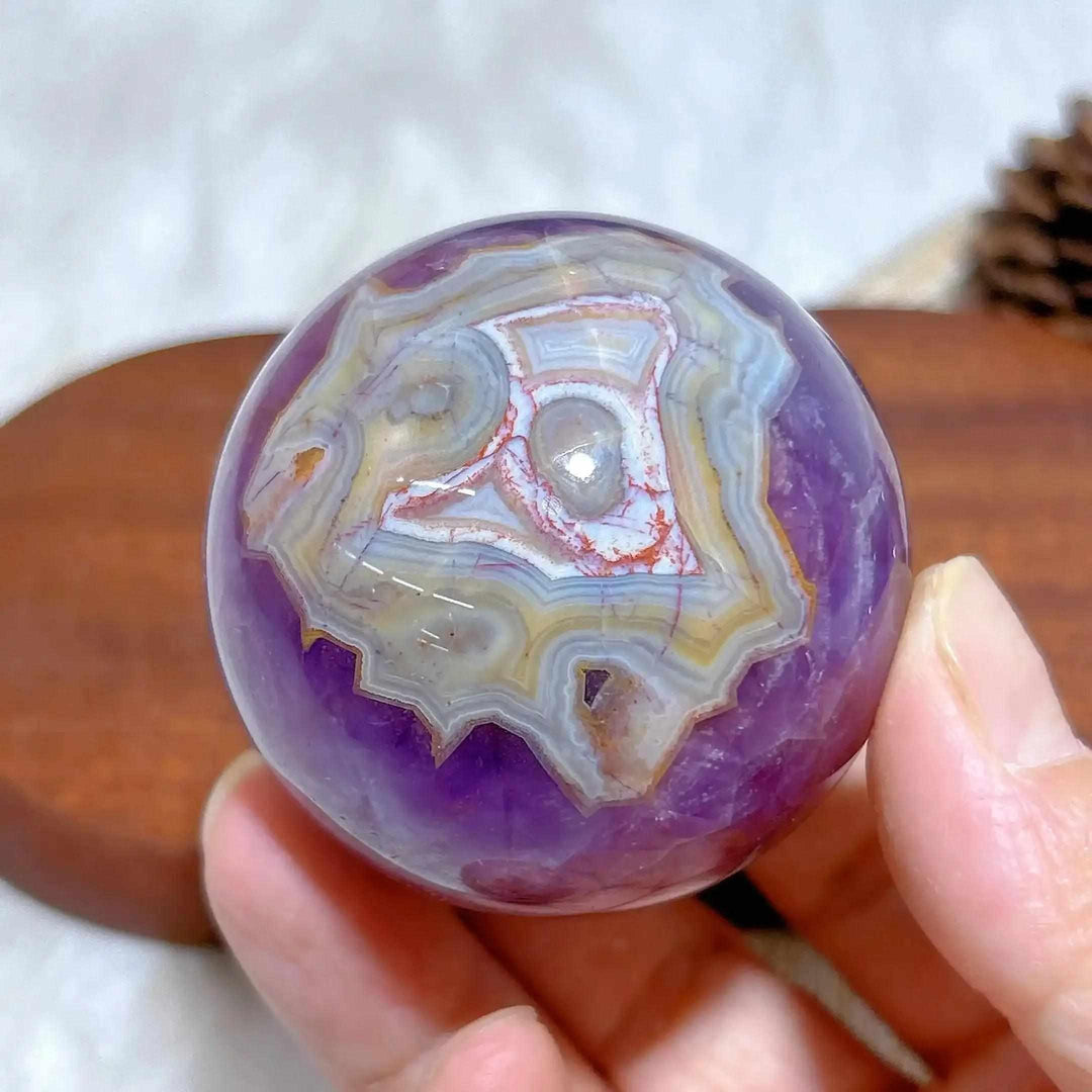 Hand-polished Amethyst Agate sphere featuring purple hues and intricate white, gray, and brown banded patterns for meditation.