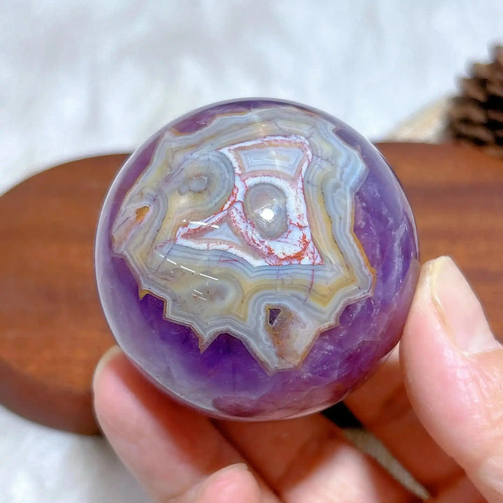 Hand-polished Amethyst Agate sphere featuring purple hues and intricate white, gray, and brown banded patterns for meditation.