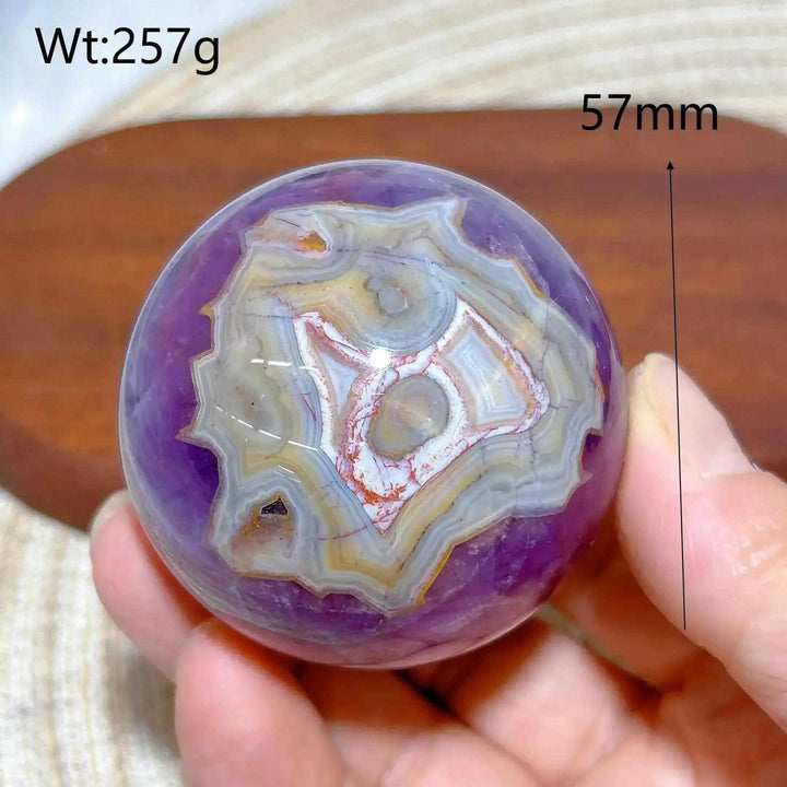 Hand-polished 57mm Amethyst Agate sphere featuring purple hues and banded white, gray, and brown patterns for calm focus.