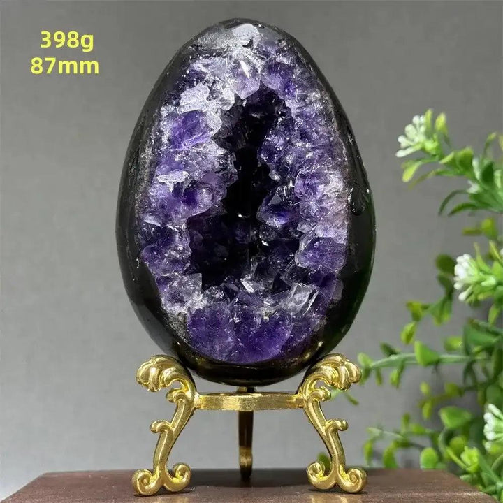 Amethyst geode dinosaur egg with sparkling purple crystals for Crown Chakra healing, displayed on a gold stand.