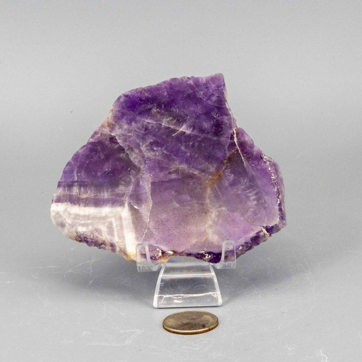 Polished purple Amethyst Slice from Crystal Destiny, displayed on a stand with a coin for scale, promoting peace.