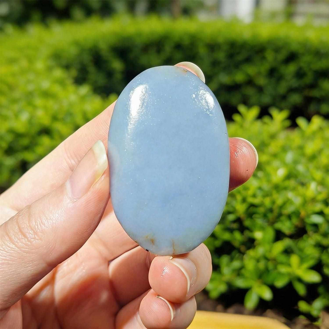 Smooth, polished blue Angelite palm stone held in hand, perfect for calming meditation and peaceful home decor.