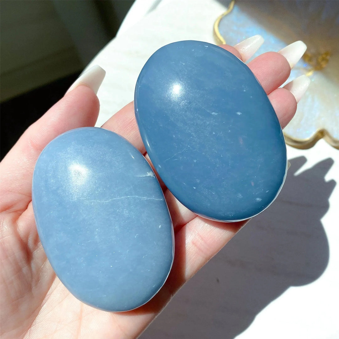 Two smooth, polished blue Angelite palm stones held in a hand, perfect for calming meditation and home decor.
