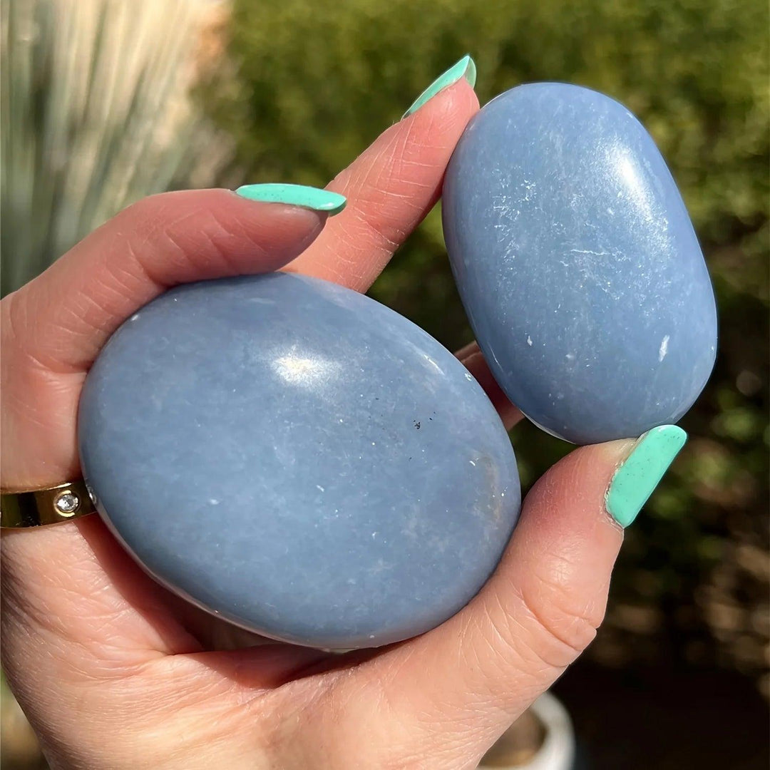 Two smooth, powder blue Angelite Crystal Polished Palm Stones held in a hand for calming anxiety relief.