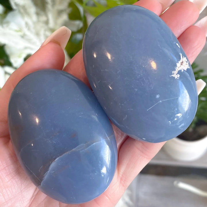 Two polished Angelite Crystal Palm Stones in powder blue, held in a hand for calming anxiety relief.
