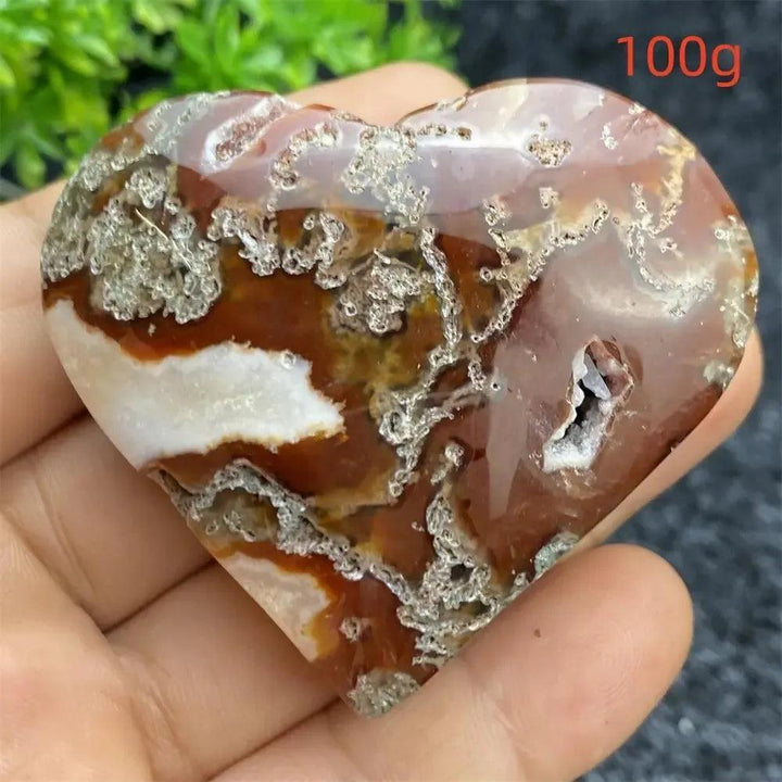 Polished red, white, and brown Aquatic Agate geode heart with sparkling druzy cavity, held in a hand.