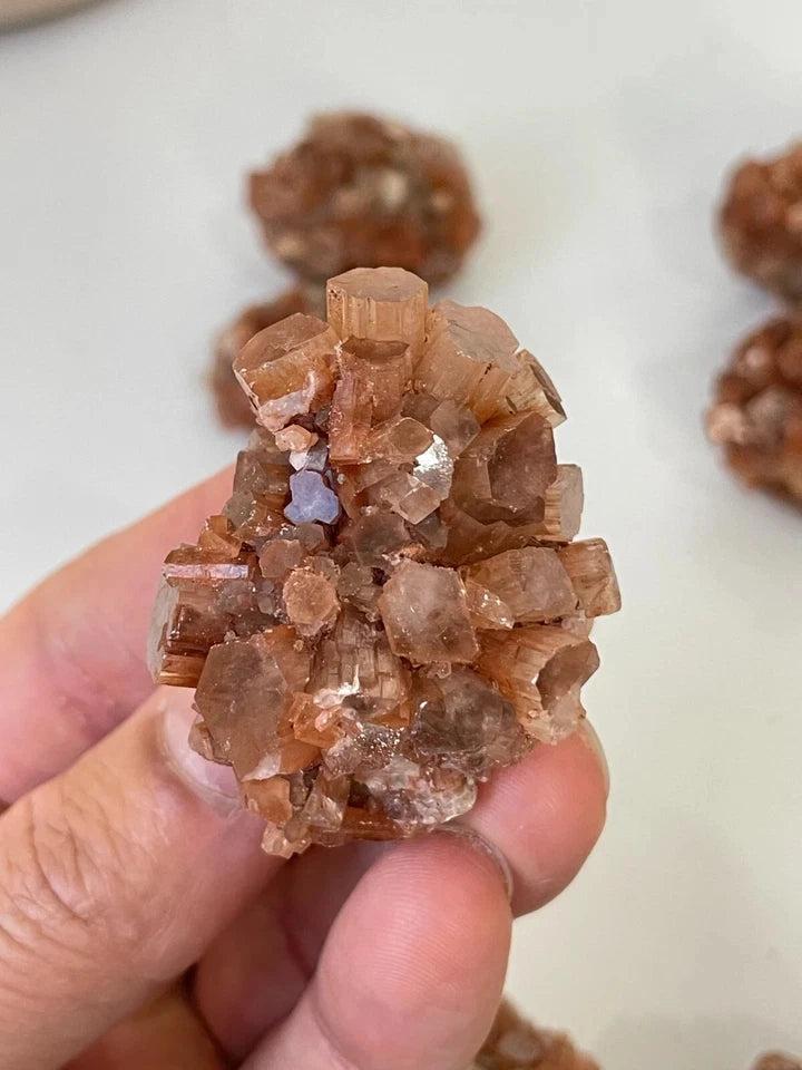 Hand holding a raw, earthy orange Aragonite "Sputnik" crystal cluster from Morocco, prized for grounding energy.