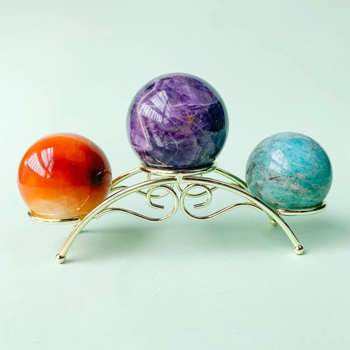 Golden arch display stand holding orange carnelian, purple amethyst, and blue amazonite crystal spheres.