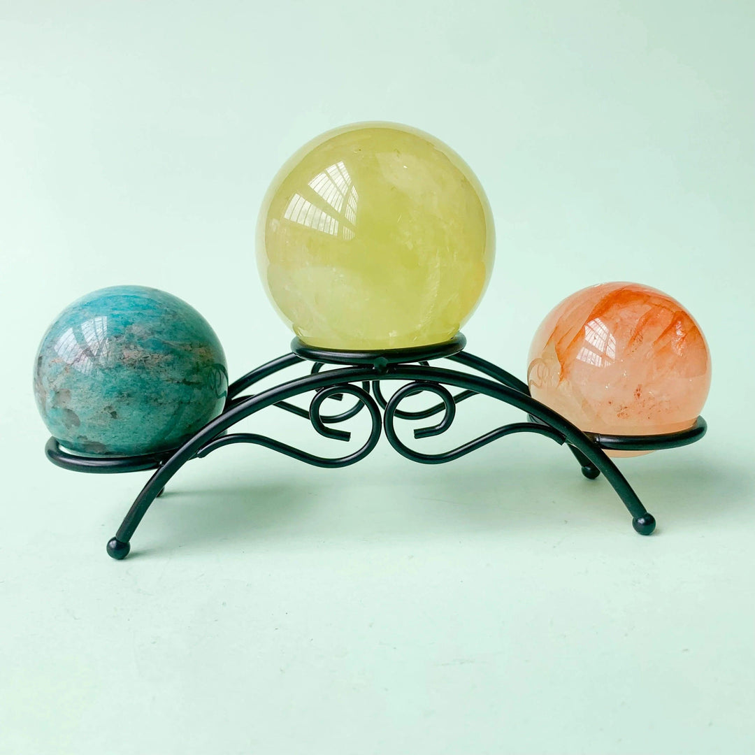 Black arch crystal display stand holding three polished crystal spheres: blue, yellow, and orange.