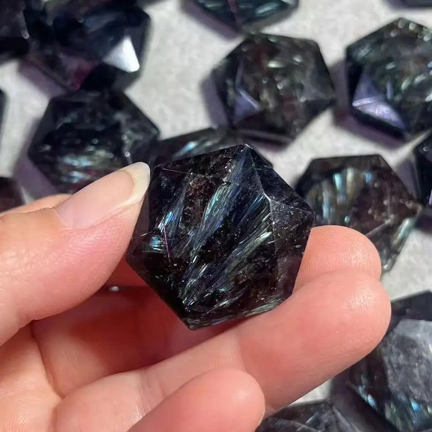 Hand holding a dark blue Arfvedsonite crystal with silver and gold flashes, carved into a faceted shape.