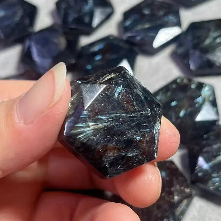 Hand holding a dark navy Arfvedsonite crystal with silver, gold, and blue flashes, carved into a five-pointed star.