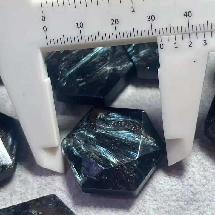 Arfvedsonite crystal, deep navy blue with silver, gold, and blue flashes, measured by a caliper.