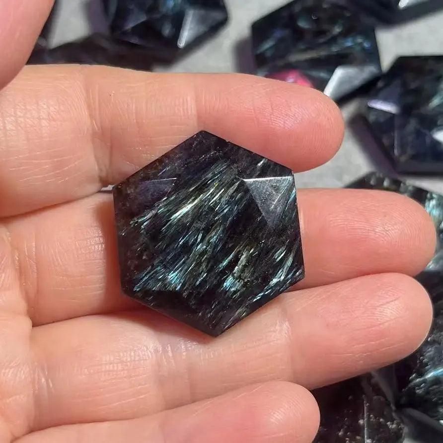 Dark blue Arfvedsonite crystal with silver and blue flashes, carved into a faceted hexagon shape, held in a hand.